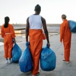 Three People in Orange Overall Holding Blue Plastic Bags